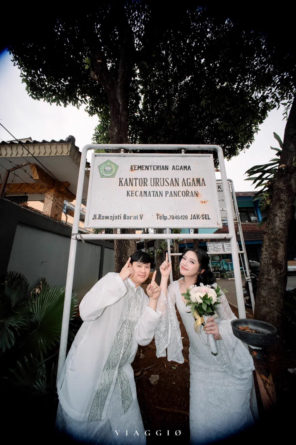 Pasangan playful di depan papan nama KUA