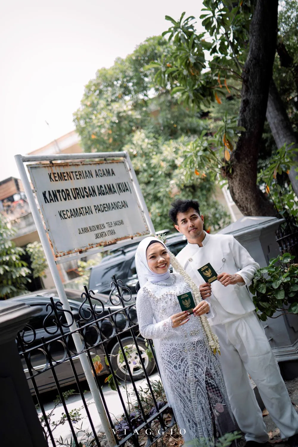 Pasangan dengan buku nikah di depan papan KUA Pademangan